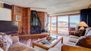 A living room with a brick fireplace, a flat-screen TV, a sofa, and a view of the outdoors.