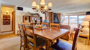 A dining area with a wooden table and chairs, a chandelier, a bookshelf, and a view of the outdoors.
