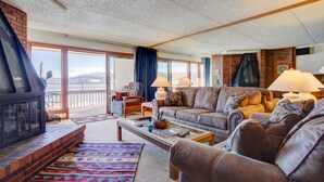 A cozy living room with a fireplace, a large sofa, and a view of the mountains through the sliding glass doors.