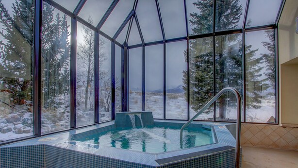 A glass-enclosed hot tub with a view of a snowy landscape.