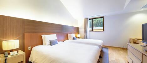 A hotel room with two beds, a desk, a TV, and a window with curtains.