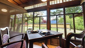 A dining area with a wooden table and chairs, large windows, and a view of the garden. - Hakone Suishoen (Hakone)