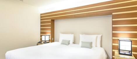 Une chambre d’hôtel avec un grand lit, une tête de lit en bois, des tables de chevet avec des lampes et une fenêtre avec des stores.