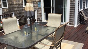 Een terras buiten met een tafel met glazen blad, zachte stoelen en een beige parasol.