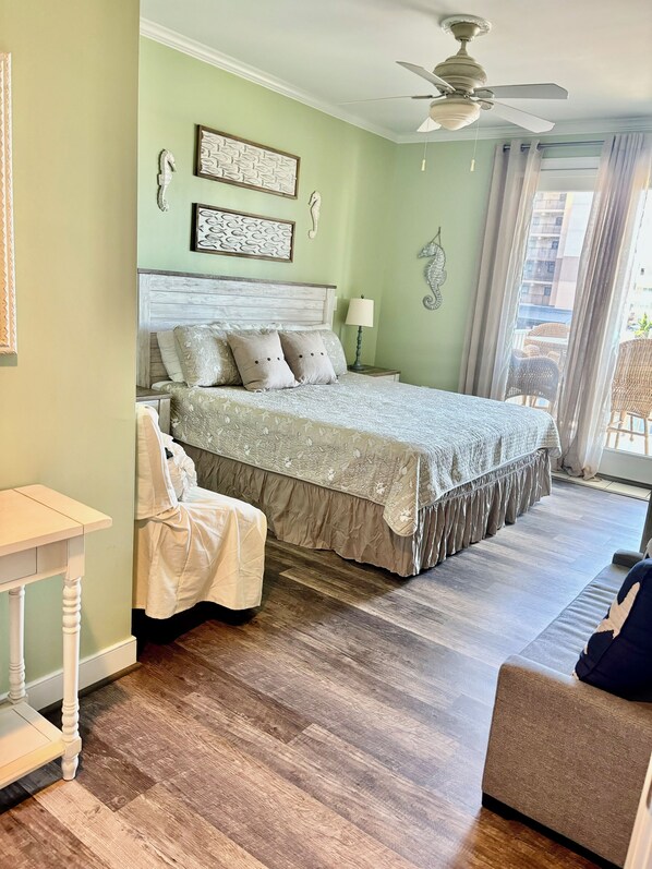 A bedroom with a bed, a chair, a nightstand, a ceiling fan, and a view of the outside. - ADAGIO BEAUTIFUL 3 BED,3 BATH OCEAN BLOCK CONDO with INDOOR POOL, STEPS TO BEACH (Ocean City)