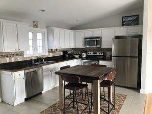 A kitchen with white cabinets, a black countertop, a wooden dining table with four chairs, a stainless steel refrigerator, and a microwave above the stove.