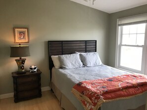 A bedroom with a bed, a nightstand, a lamp, and a window.