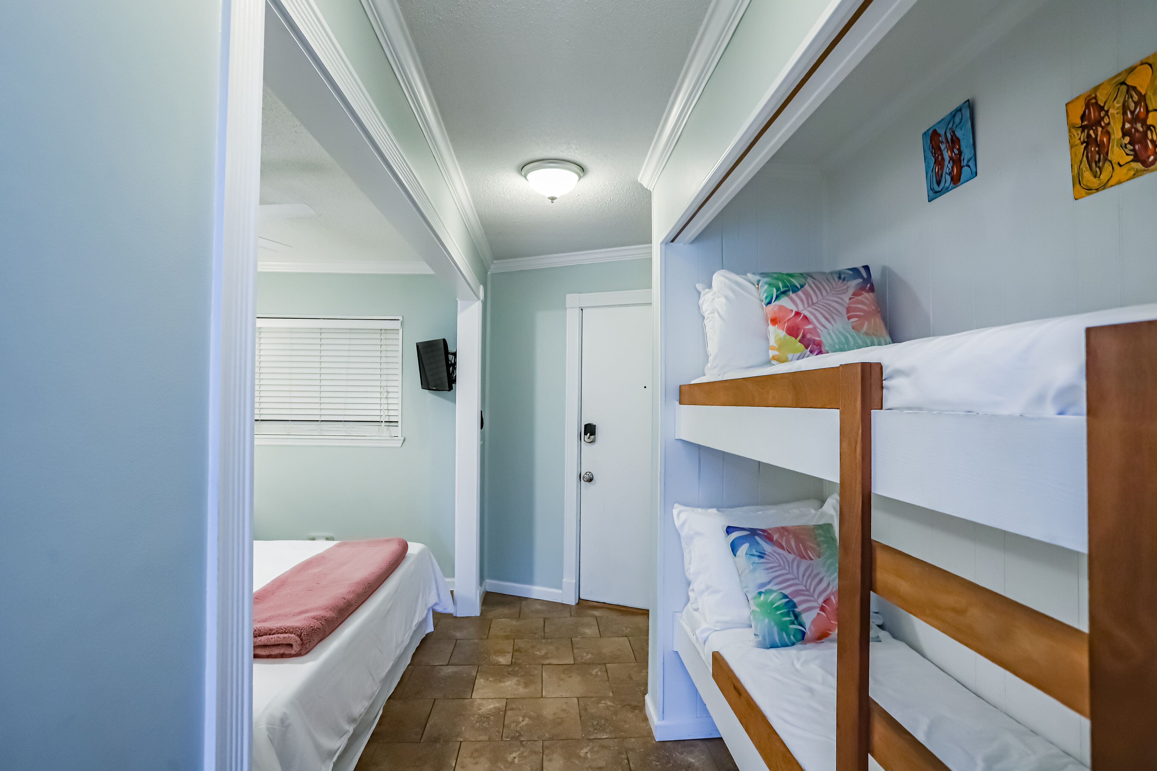 A narrow hallway with bunk beds on the right, a door at the end, and a bed with a pink blanket on the left.