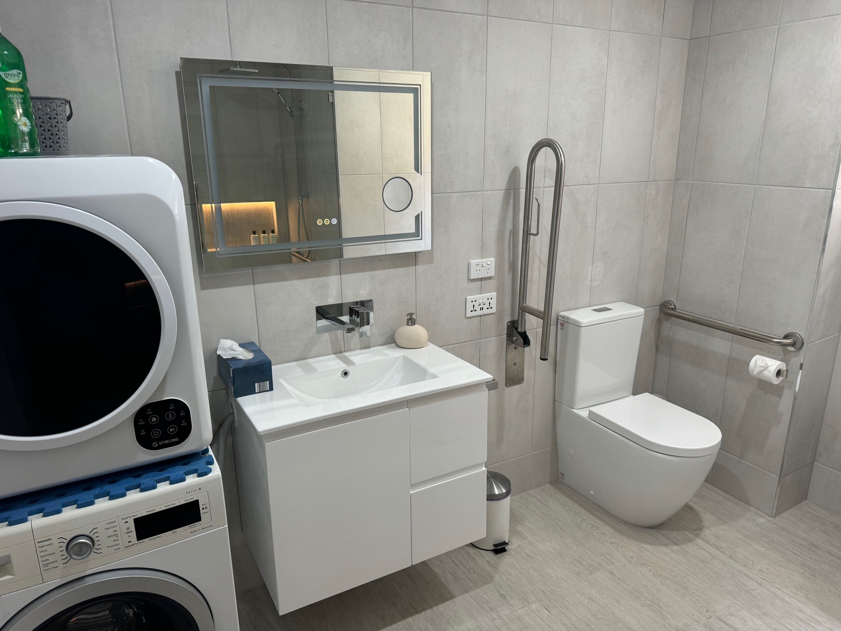 Un baño moderno con lavadora integrada, lavamanos, inodoro y zona de ducha.