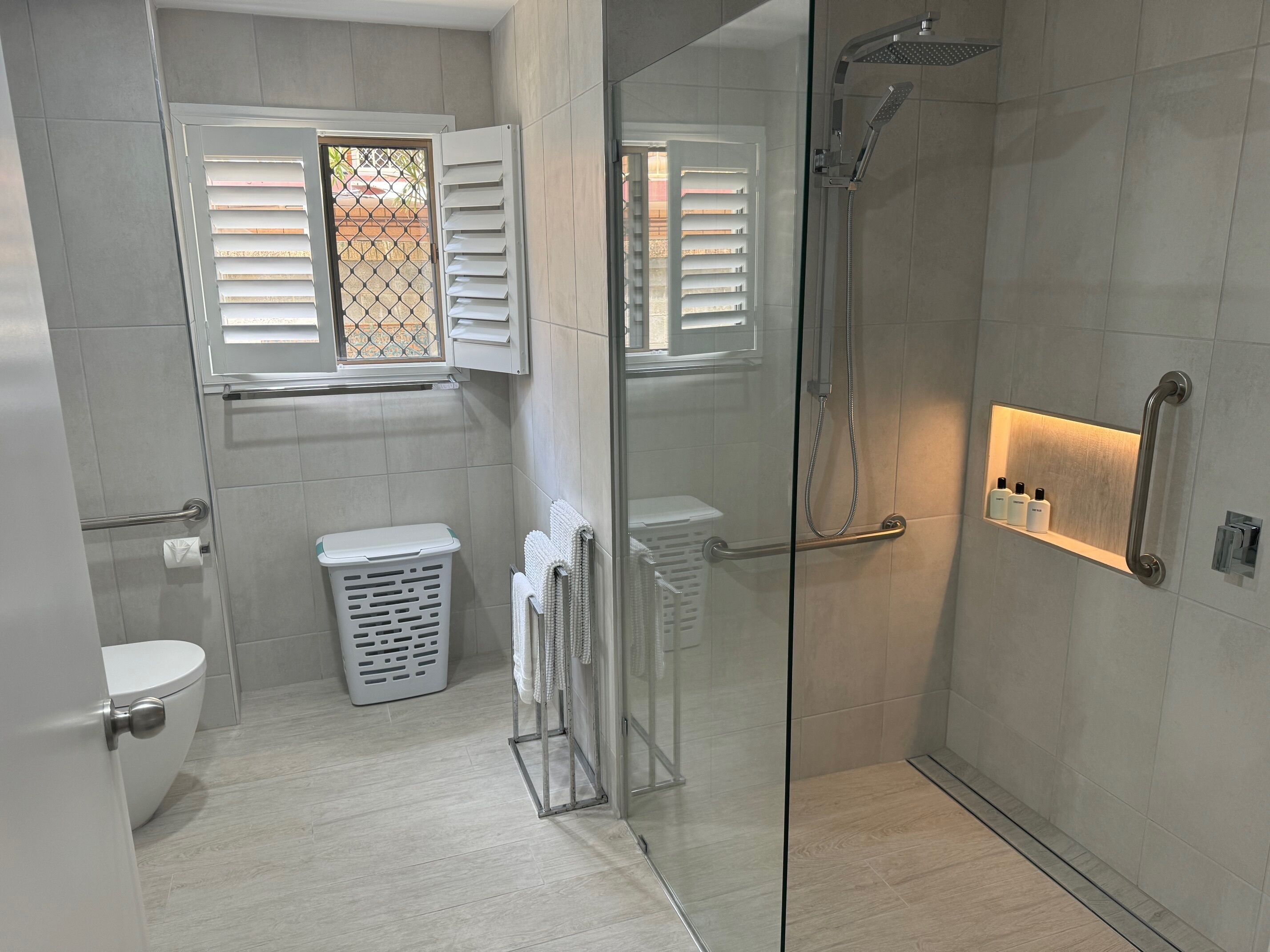Une salle de bain moderne avec une douche à parois de verre, des toilettes, un panier à linge et un porte-serviettes.