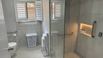 A modern bathroom with a glass shower enclosure, a toilet, a laundry basket, and a towel rack.