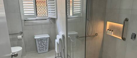 Une salle de bain moderne avec une douche à parois de verre, des toilettes, un panier à linge et un porte-serviettes.