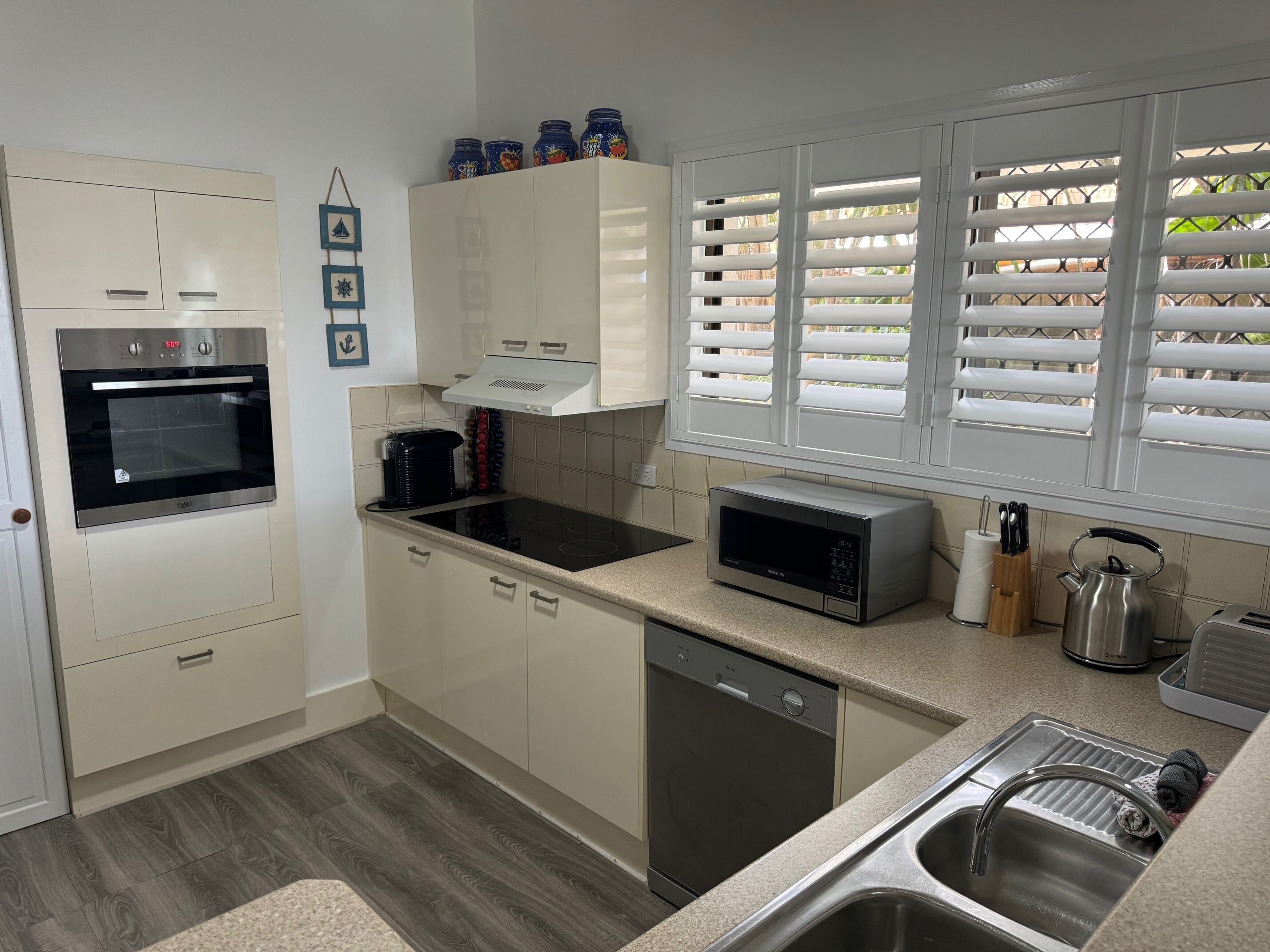 A modern kitchen with a built-in oven, microwave, and dishwasher. There are cabinets, a countertop, and a window with blinds.