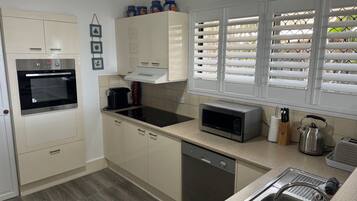 A modern kitchen with a built-in oven, microwave, and dishwasher. There are cabinets, a countertop, and a window with blinds.