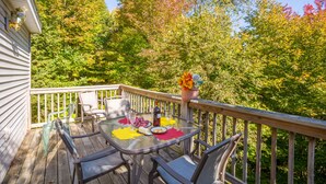A wooden deck with a glass table and chairs, surrounded by trees with autumn foliage. -  Resort Mountain Home with  Private Hot tub Walk to Pools, Pond WIFI (Campton)