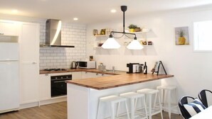 Una cocina moderna con armarios blancos, una isla de madera con taburetes de bar, una campana extractora de acero inoxidable e iluminación colgante.