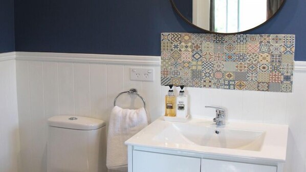 Un baño con lavamanos blanco, espejo y salpicadero de azulejos estampados.
