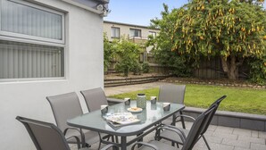 Een terras buiten met een glazen tafel en stoelen, een krant en een decoratieve vaas.