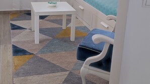 A small, well-lit room with a bed, a white table, and a blue chair.