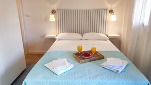 A neatly made bed with a light blue quilt, two bedside lamps, a tray with fruit and juice, and two towels on the bed.