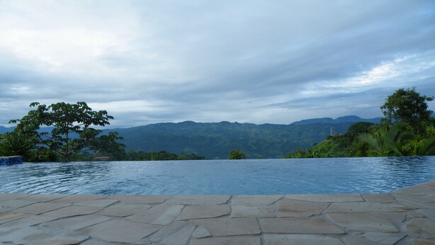 A stone-tiled infinity pool with a view of mountains and greenery. - Luxurious Castle, Infinity Pool And Jaw Dropping Views!  (Atenas)