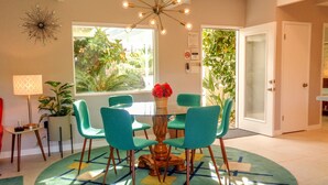 A dining area with a round table, teal chairs, a chandelier, and a patterned rug. - PS-ID #76 Stylish Mid-Century Modern Oasis with Surrounding Mountain Views (Palm Springs)