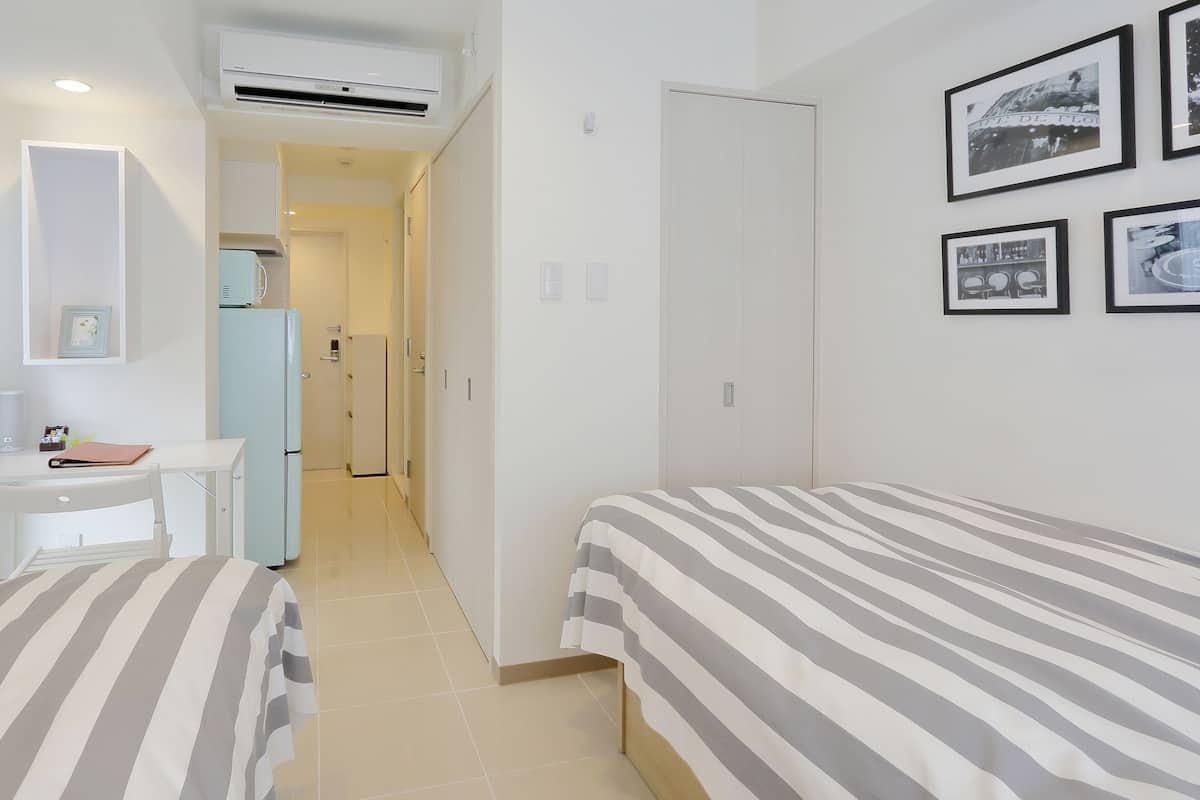 A hotel room with two single beds, a desk, a chair, a small table, a refrigerator, and a wardrobe.