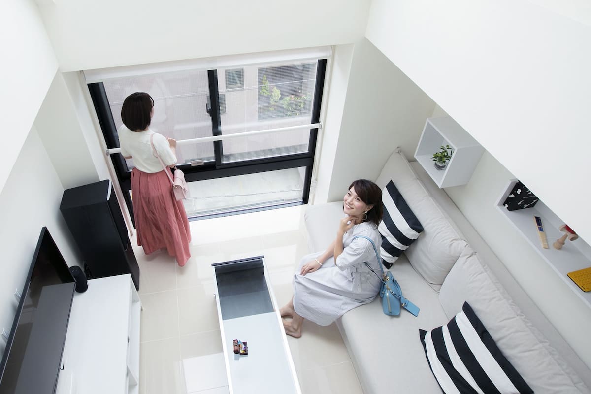 A modern living room with a large window, a sofa, a TV, and a small table.