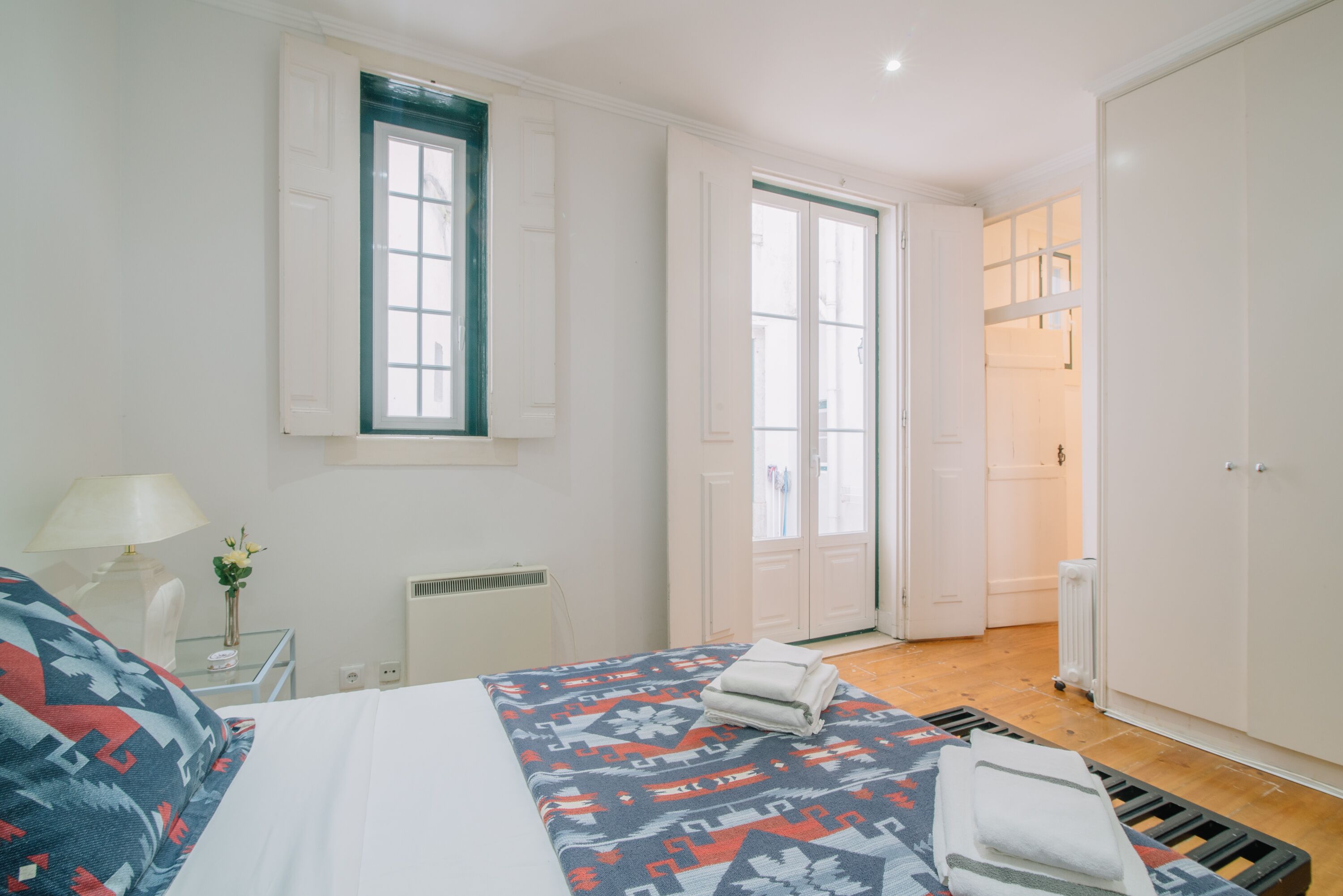 A hotel room with a bed, a bedside table with a lamp, a window, and a wardrobe.