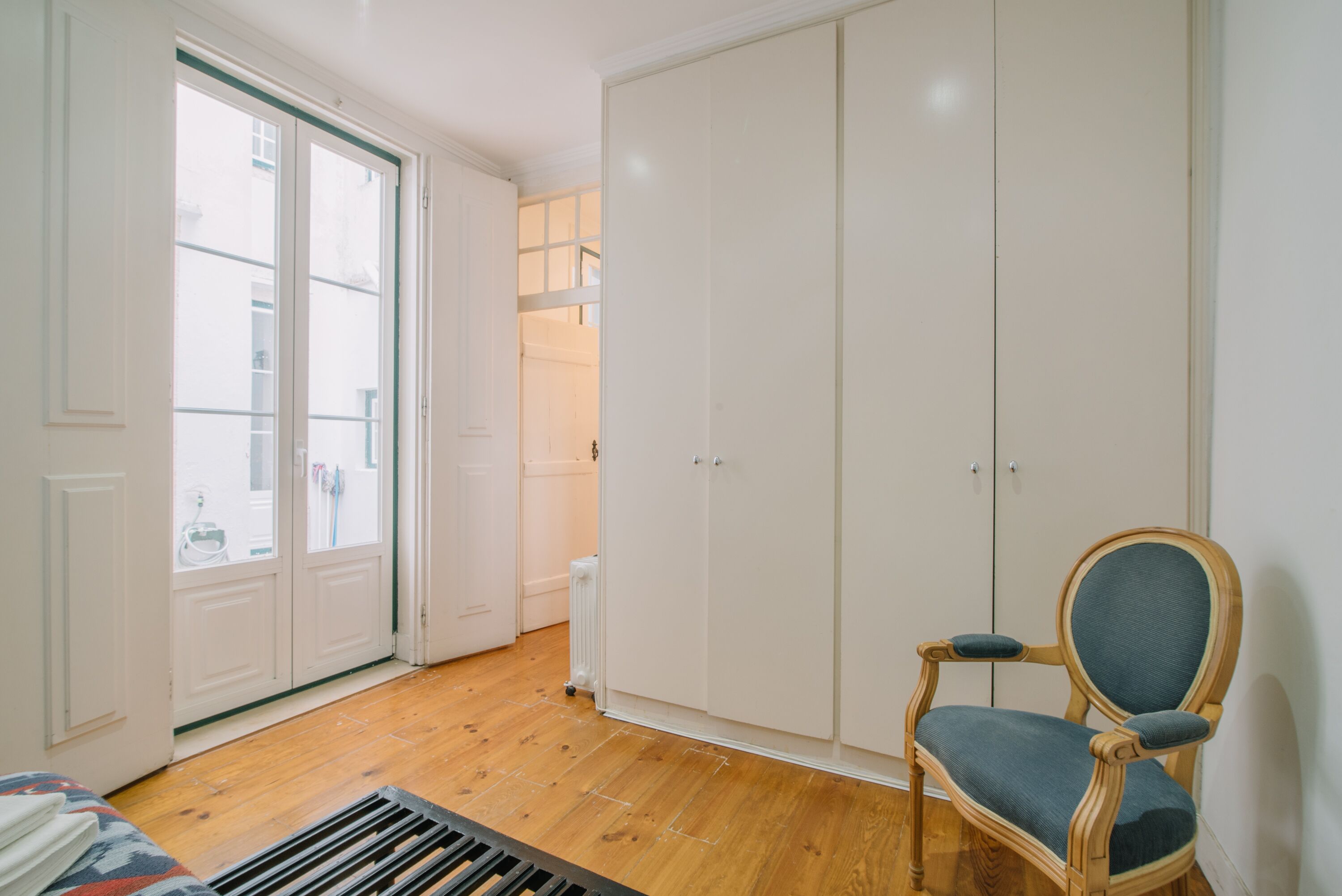 A room with a wooden floor, a blue upholstered chair, and a white wardrobe with two doors.
