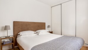 A neatly made bed with a patterned blanket, two bedside lamps, a wooden nightstand, and a sliding door to the right. - Chiado | STYLISH & GREAT VIEW | Family-Friendly (Lisboa)