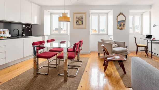 A modern apartment with a kitchen, dining area, and living room. It features white cabinetry, red chairs, and a grey sofa. - Chiado | STYLISH & GREAT VIEW | Family-Friendly (Lisboa)