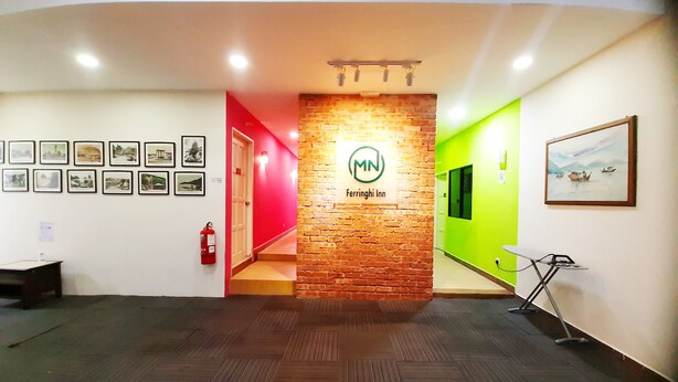 A hotel lobby with a brick wall, a sign for 'Ferrighi Inn', and a green wall with a painting. - MN Ferringhi Inn (George Town)