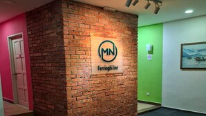 A brick wall with a logo and the name "Ferrinho Inn" in a hallway with a green door and a framed picture on the wall. - MN Ferringhi Inn (George Town)