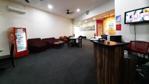 A reception area with a wooden counter, seating area with couches and chairs, a refrigerator, and a television on the wall. - MN Ferringhi Inn (George Town)