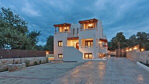 Ein modernes, zweistöckiges Haus mit Naturstein-Fassade, mehreren Balkonen und einer gepflasterten Auffahrt.