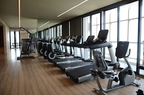 Een sportschool met loopbanden, elliptische trainers en gewichtstoestellen, allemaal opgesteld in een rij.