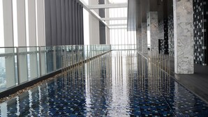 Et moderne poolområde indendørs med glasgelændere og flisegulv.