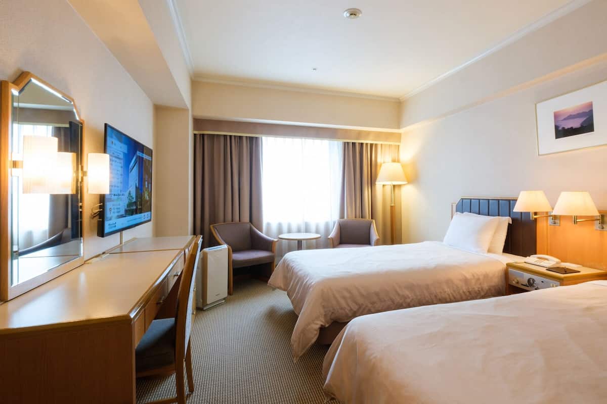 Une chambre d’hôtel avec deux lits, un bureau, une chaise, une télévision et une fenêtre avec des rideaux.