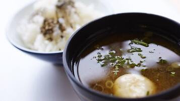 A bowl of clear soup with a boiled egg and green onions, accompanied by a bowl of white rice with brown seasoning.