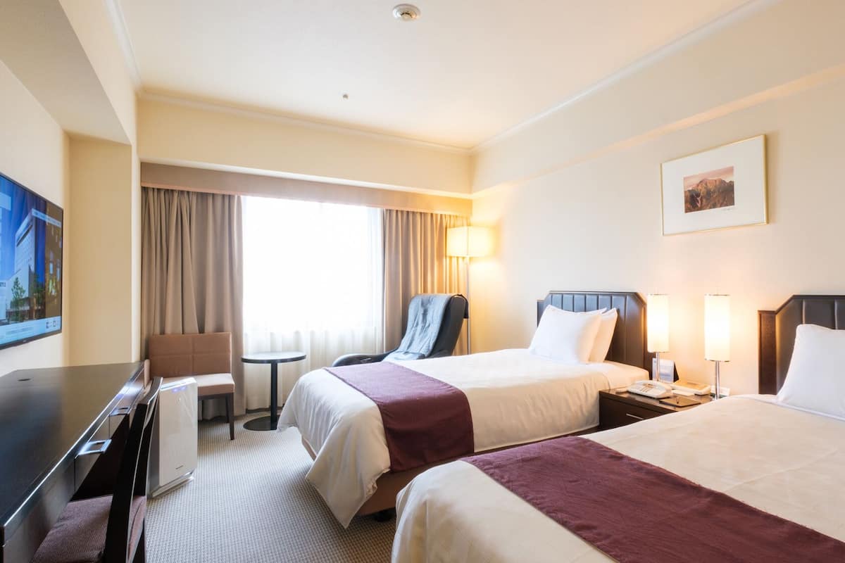 Une chambre d’hôtel avec deux lits, un bureau, une chaise, une lampe et un tableau au mur.