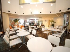 Un restaurante moderno con mesas redondas y sillas blancas, que presenta una zona de bar central y ventanas amplias.