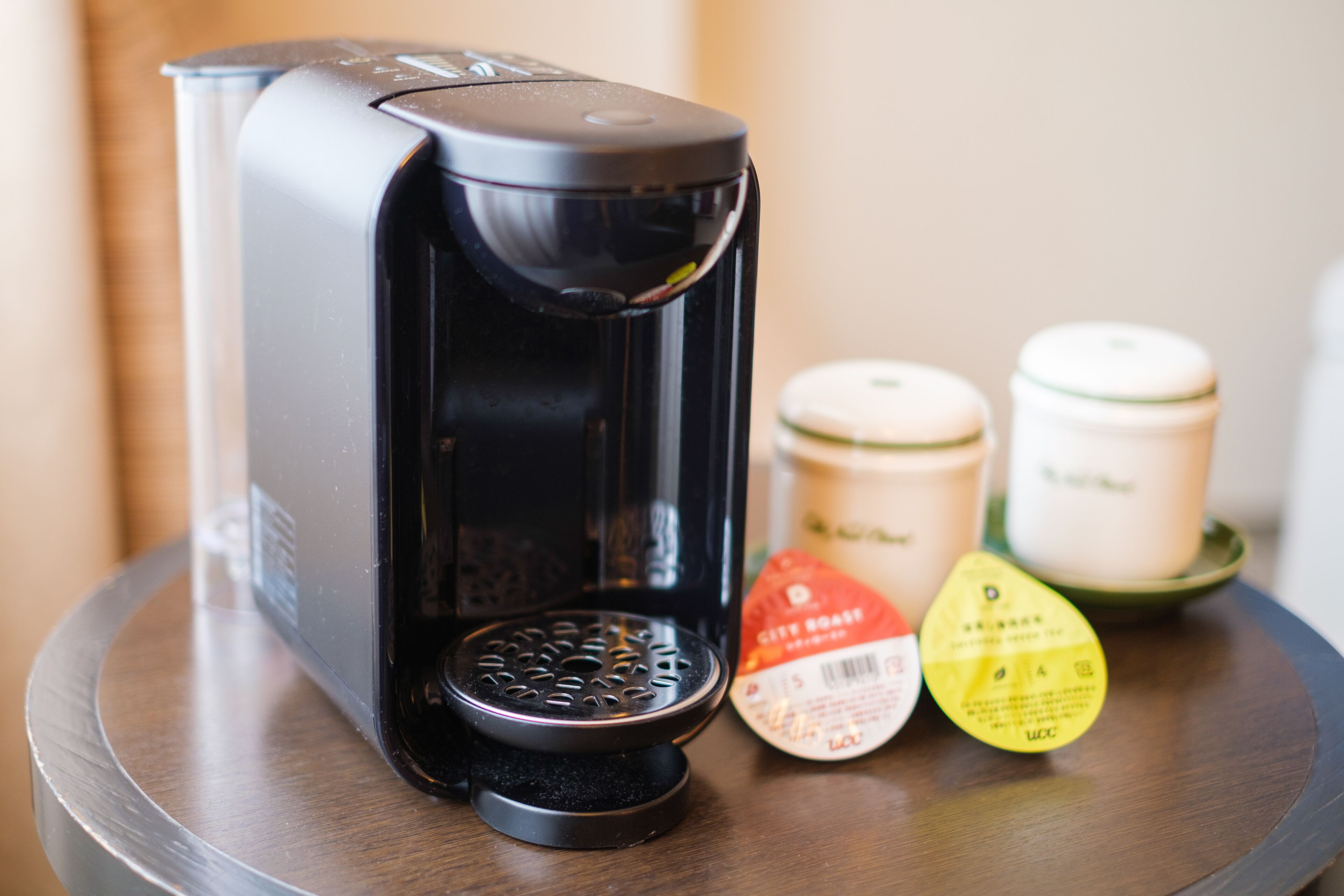 A coffee maker with a drip tray and two containers on a wooden table.