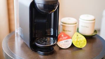A coffee maker with a drip tray and two containers on a wooden table.