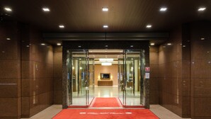 L’entrée d’un hôtel, avec un tapis rouge, des portes en verre et un espace de réception agrémenté d’un lustre.