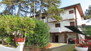 A multi-story building with balconies, surrounded by trees and potted plants. - Stay near the beach and thermal area (Bibione)