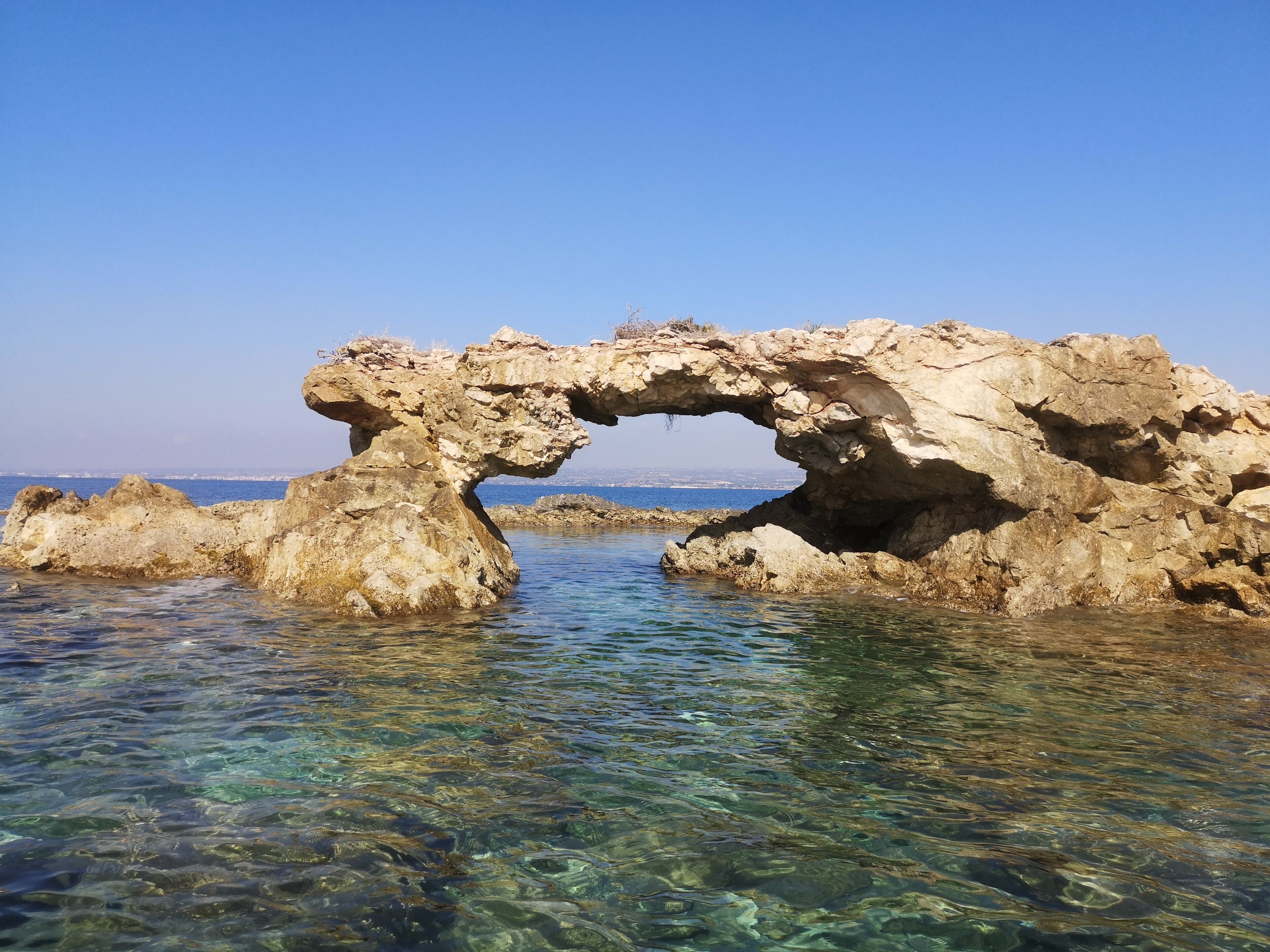Una formazione rocciosa naturale con una piscina di acqua limpida di fronte.