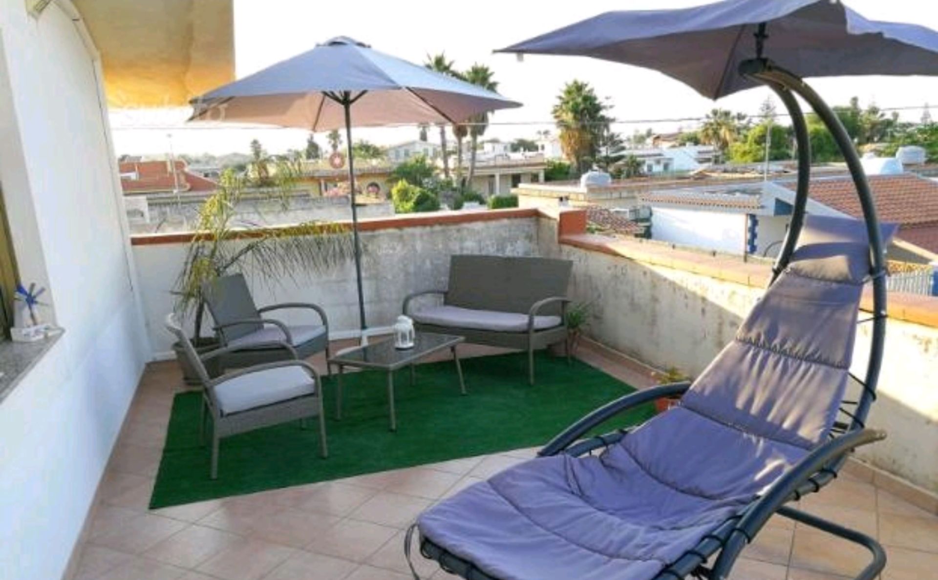 En tagterrasse med en klapstol, to sofaer, et lille bord og to parasoller.