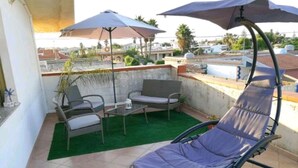 Eine Dachterrasse mit einem Klappsessel, zwei Sofas, einem kleinen Tisch und zwei Sonnenschirmen.