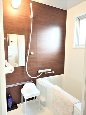 Ein modernes Badezimmer mit einer Holzvertäfelung, einer weißen Badewanne, einem kleinen weißen Hocker und einem Handtuch, das an der Wanne hängt.